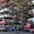 Numerous stacked rows of disassembled cars are placed on metal structures in what appears to be a scrapyard. Many of the cars are missing parts like wheels and doors.